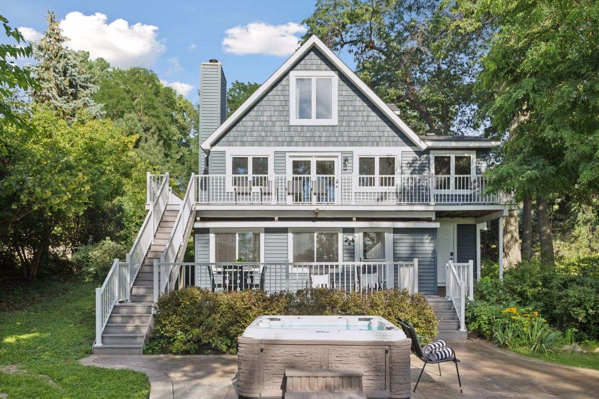Charming lakeside retreat featuring multi-level decks and a private hot tub, nestled among towering trees. The spacious exterior offers plenty of room to unwind and soak in the peaceful natural surroundings.