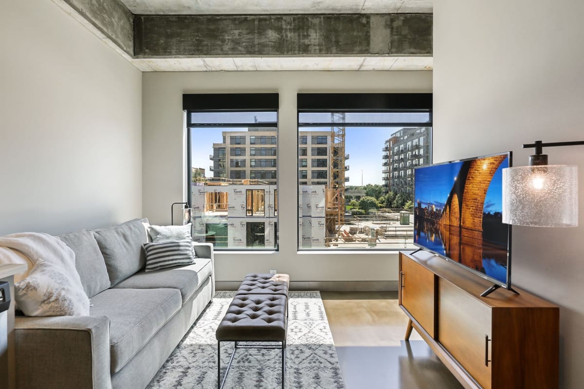 Unwind in your contemporary living space featuring industrial-chic details and floor-to-ceiling windows showcasing vibrant city views.