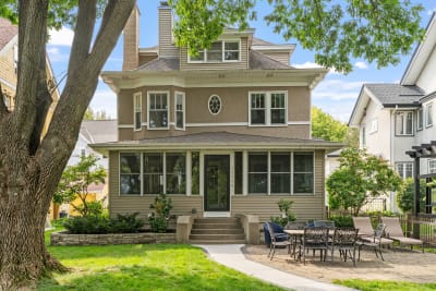A beautiful two-story house with a porch, large windows, and outdoor patio furniture.