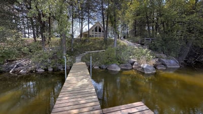 Lakeside scene with a wooden dock leading to a modern house surrounded by trees.
