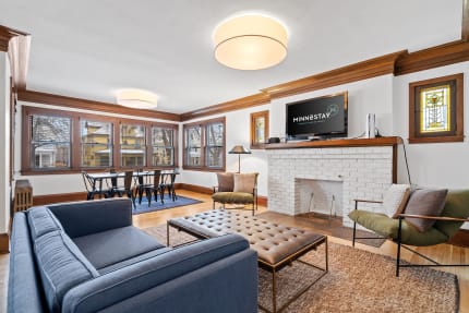 A bright living room with a blue couch, a coffee table, and a dining area with windows.