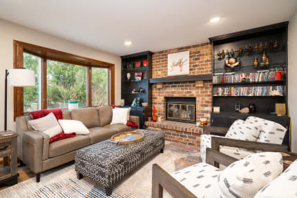 A comfortable living room with a beige leather sofa, patterned ottoman, and black shelving unit.