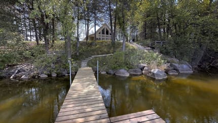 Lakeside scene with a wooden dock leading to a modern house surrounded by trees.