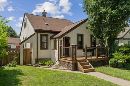 Cozy home with a front porch, green lawn, and blue sky in a peaceful neighborhood.