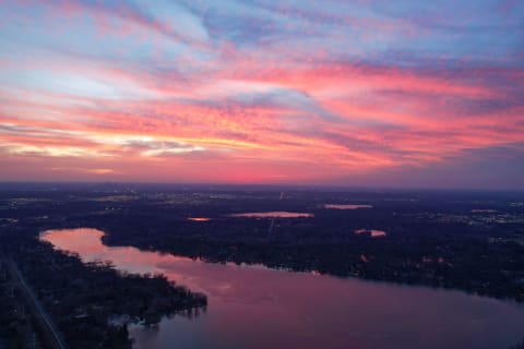 Aerial view of a sunset with pink and purple skies reflected on a lake and city lights in the distance.