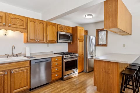A cozy kitchen with wooden cabinetry, stainless steel appliances, and a casual dining area with stools.