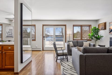 A bright living room featuring lake views through French doors, gray sofas, and a black armchair.