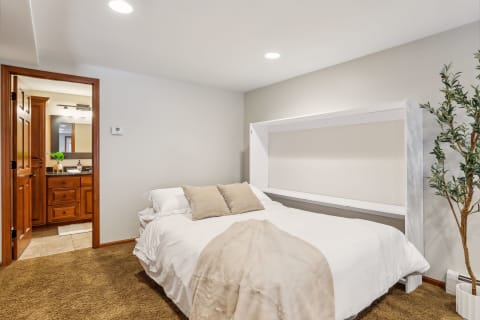 A cozy bedroom featuring a plush bed with white linens, decorative pillows, and a touch of greenery from a nearby plant.