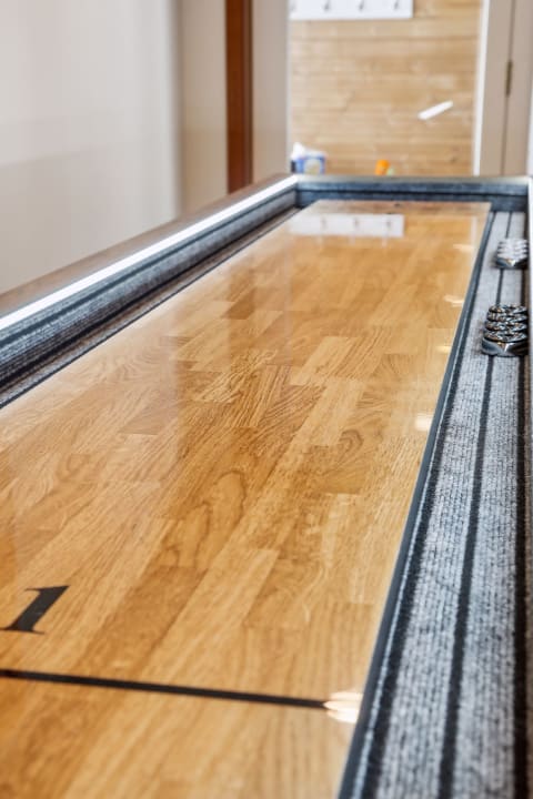A polished shuffleboard table with a wooden surface and dark carpet edges, ready for a game.