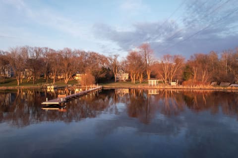 A peaceful lakeside neighborhood with wooden docks extending into calm water surrounded by homes and trees.