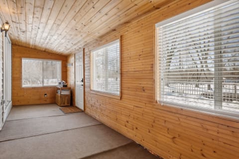A screened porch with wood paneling, large windows, and a cozy atmosphere.