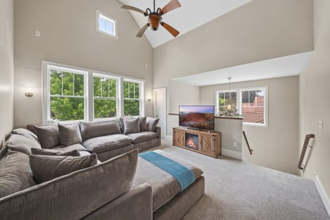 Cozy living room with a sectional couch, vaulted ceilings, and large windows overlooking greenery.