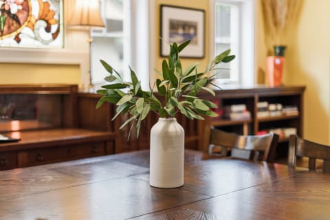 A vase with green leaves on a wooden dining table in a warmly lit room.