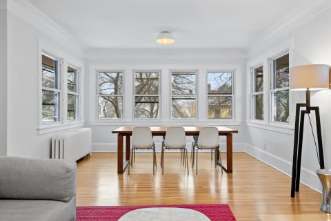 Cozy dining room with wooden table, white chairs, and natural light from multiple windows.