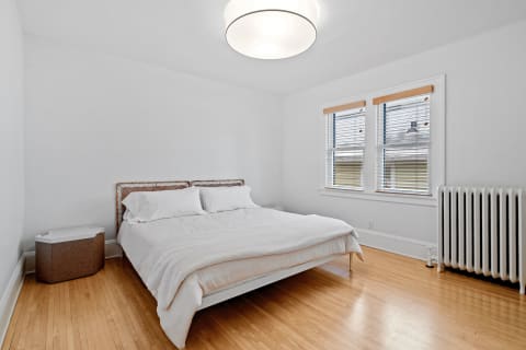 Minimalist bedroom with white walls, a rattan bed frame, and natural light from windows.