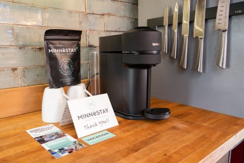 A kitchen countertop displaying a Nespresso coffee maker, coffee bags, mugs, and knives on a wall.