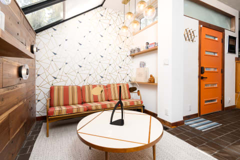 Modern living space featuring a colorful sofa, geometric wall art, and an orange door.