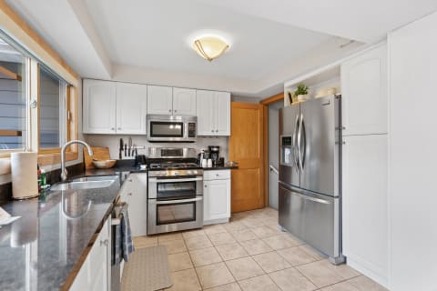 Contemporary kitchen with white cabinets, black countertop, and stainless steel appliances.