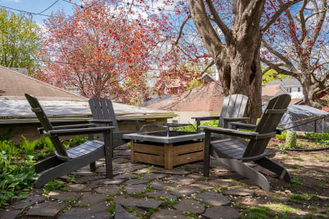Backyard seating area featuring Adirondack chairs and a fire pit with trees in the background.