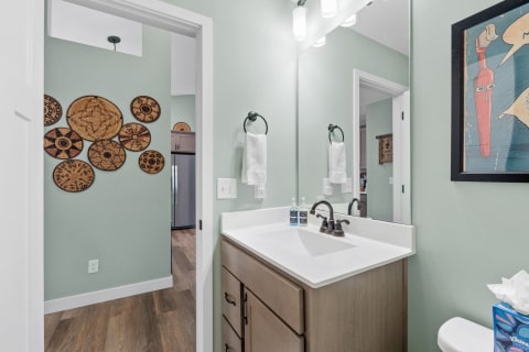 Modern bathroom with green walls, white sink, and woven art pieces on the wall.