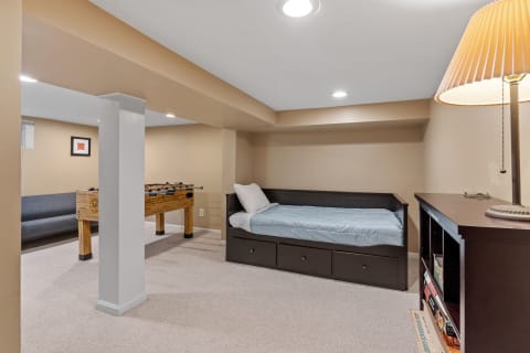 A basement room featuring a bed, a foosball table, and a sofa.