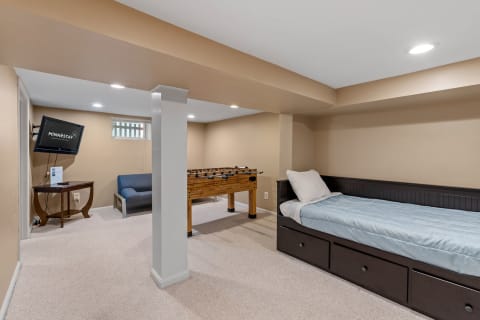 Cozy basement with a foosball table, TV, couch, and bed.