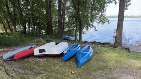 Colorful kayaks and a pedal boat lined up on the grass with a view of the lake in the background.