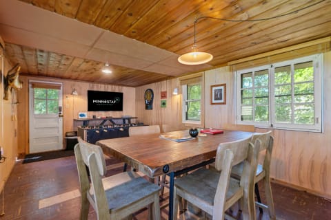 A rustic dining area with a wooden table, beige chairs, and a modern TV displaying Minnestay's logo.