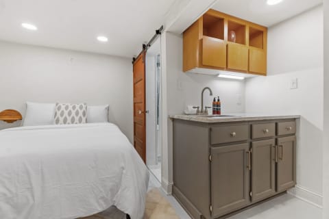 A small room featuring a bed, decorative pillow, and kitchenette with shelves.