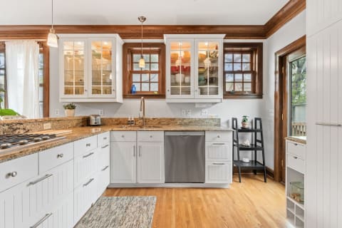 Modern kitchen with white cabinets, glass shelves, granite countertops, and a wooden floor.