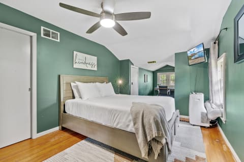 Cozy bedroom featuring a queen-sized bed, green walls, and a decorative sign.