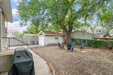 Backyard with chairs, fire pit, tree, and garage.