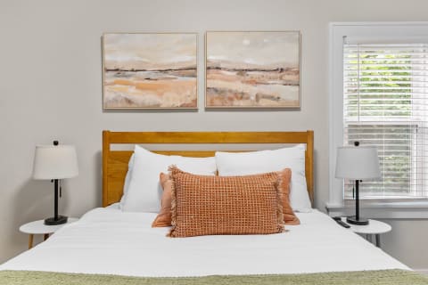 Cozy bedroom featuring a wooden bed, textured pillows, and abstract paintings.