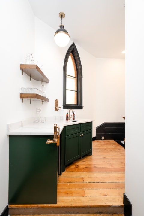 Interior view of a small kitchen featuring green cabinets, a white countertop, and an arched window.