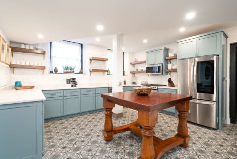 Modern kitchen featuring turquoise cabinets, wooden shelves, and a rustic table.