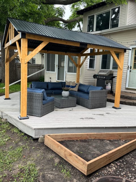 A cozy outdoor gazebo with seating and a grill in a residential backyard.