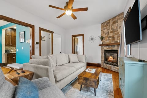 Cozy living room with a light gray sofa, stone fireplace, and blue-green cabinet.