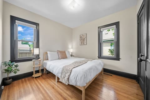 A serene bedroom featuring a cozy bed, wooden floors, and natural light from windows.