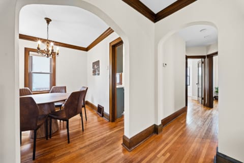 A dining space featuring a round wooden table and upholstered chairs, framed by elegant archways and natural light.
