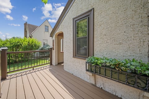A cozy corner of a house with a wooden deck and planter filled with plants against a blue sky.