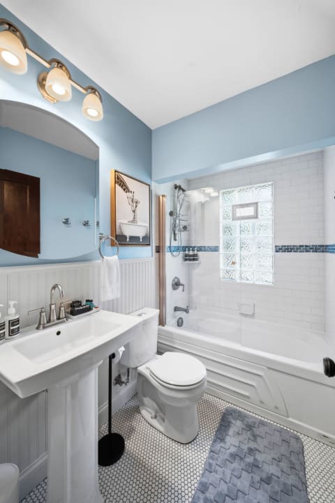 A serene bathroom with blue walls, white tiles, and a pedestal sink, complete with modern fixtures and a glass block window.