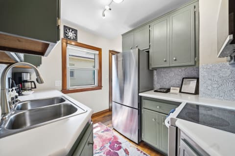 Cozy kitchen with olive green cabinets, stainless steel refrigerator, and patterned backsplash, illuminated by natural light.