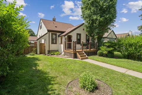 Charming home with a front deck and lush lawn surrounded by greenery.