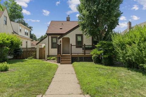 A cozy light-colored home with a wooden staircase and well-kept lawn in a quiet residential setting.