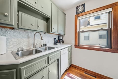 A kitchen featuring sage-green cabinets, a double sink, and a floral backsplash.
