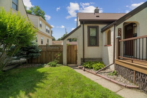 Entrance to a cozy property featuring a neat lawn, stone path, and wooden porch.