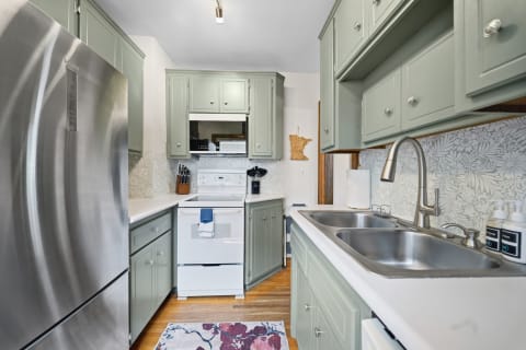 A well-equipped kitchen with sage-green cabinets, stainless steel appliances, and floral backsplash.