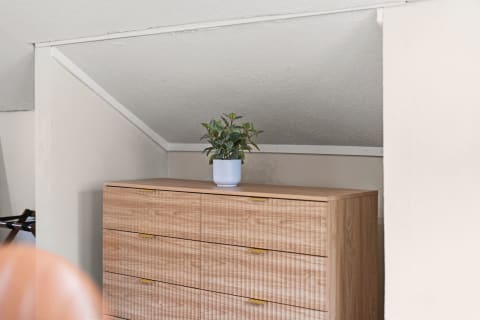 Stylish wooden dresser under a sloped ceiling with a small potted plant on top.