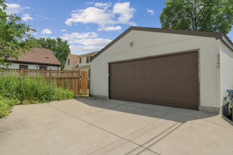 A parking pad next to a brown garage, featuring neighboring houses and greenery.