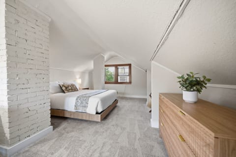 Cozy loft bedroom with vaulted ceilings and natural light, featuring a white brick column and wooden furniture.